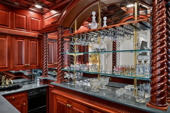 Wet bar with carved wood paneling and glass shelving